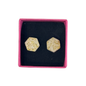 A pair of hexagonal stud earrings with a textured beige resin base and embedded gold glitter, presented in a pink box with a black velvet insert.