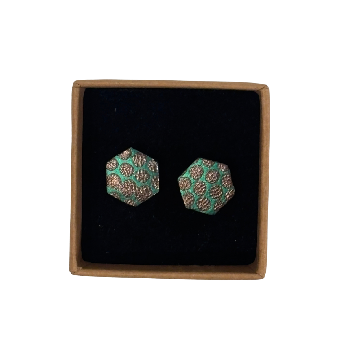 A pair of hexagonal stud earrings with a green and brown leopard print pattern, presented in a square black velvet box with a brown cardboard border on a white background.