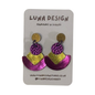A pair of handmade statement earrings by Luna Design, featuring a gold glitter stud, a textured purple glitter circle, and a split purple and gold glitter chevron, displayed on a white card backing.