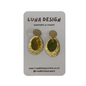 A pair of textured gold teardrop-shaped dangle earrings with flat circular gold studs, displayed on a grey card backing printed with 'LUNA DESIGN'.