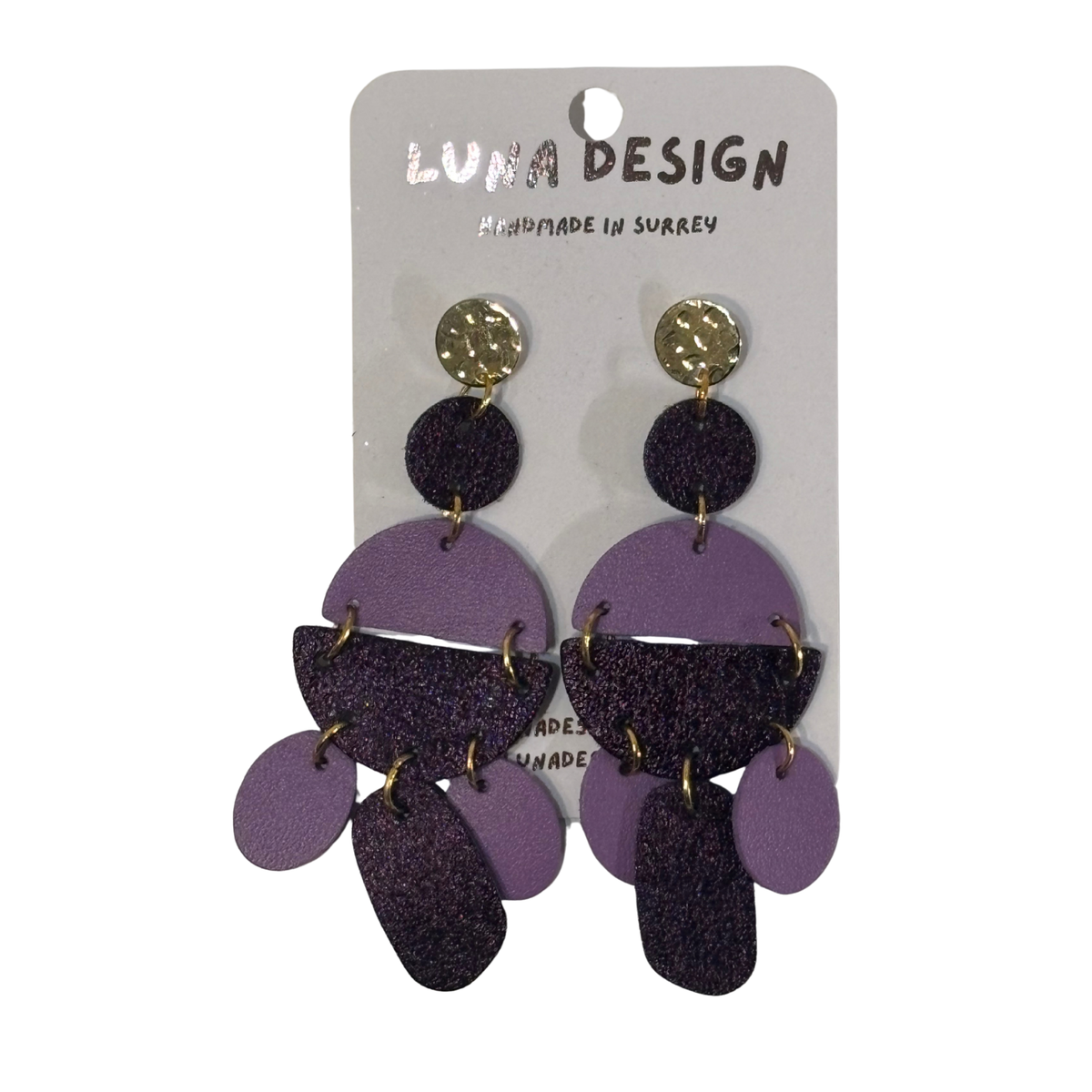 A pair of purple and black layered geometric dangle earrings with gold-tone studs, displayed on a white card labeled 'LUNA DESIGN'.