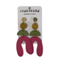 A pair of handmade statement earrings by Luna Design, featuring a gold-tone top stud with a textured gold disc, a green semicircle, and a large textured magenta U-shaped drop. The earrings are displayed on a white cardboard backing card that reads 'LUNA DESIGN HANDMADE IN SURREY'.