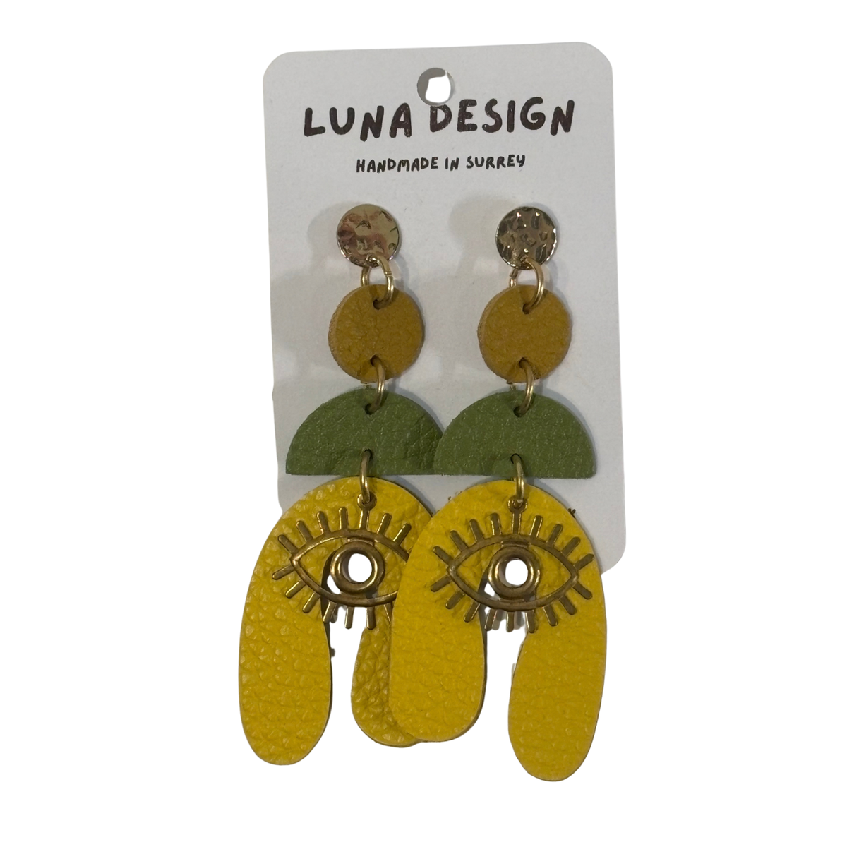 A pair of multi-layered dangle earrings by Luna Design, featuring yellow and green geometric shapes with gold-tone eye details, displayed on a white backing card.