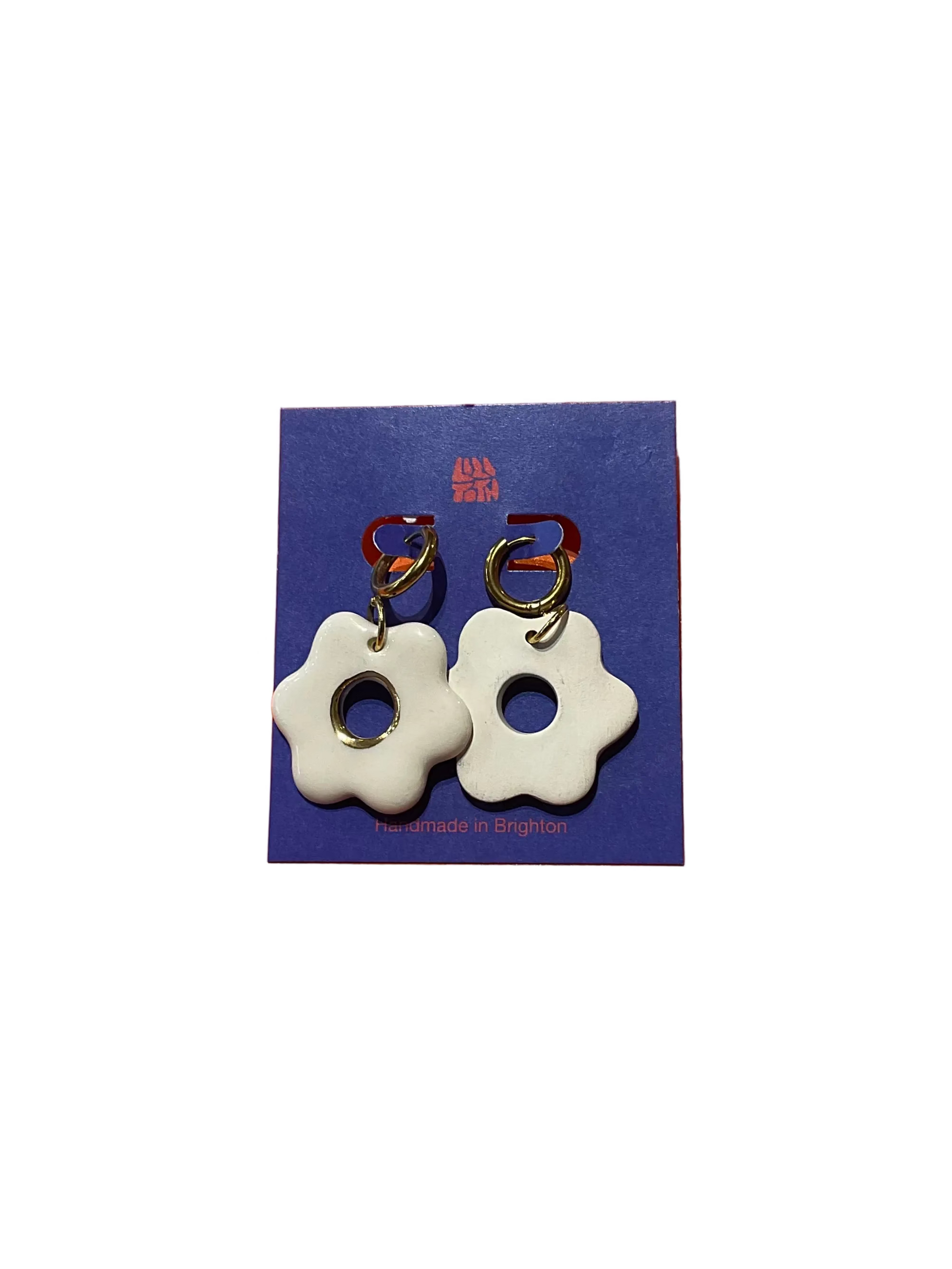 White flower-shaped earrings on a blue card with a visible brand logo against an orange background