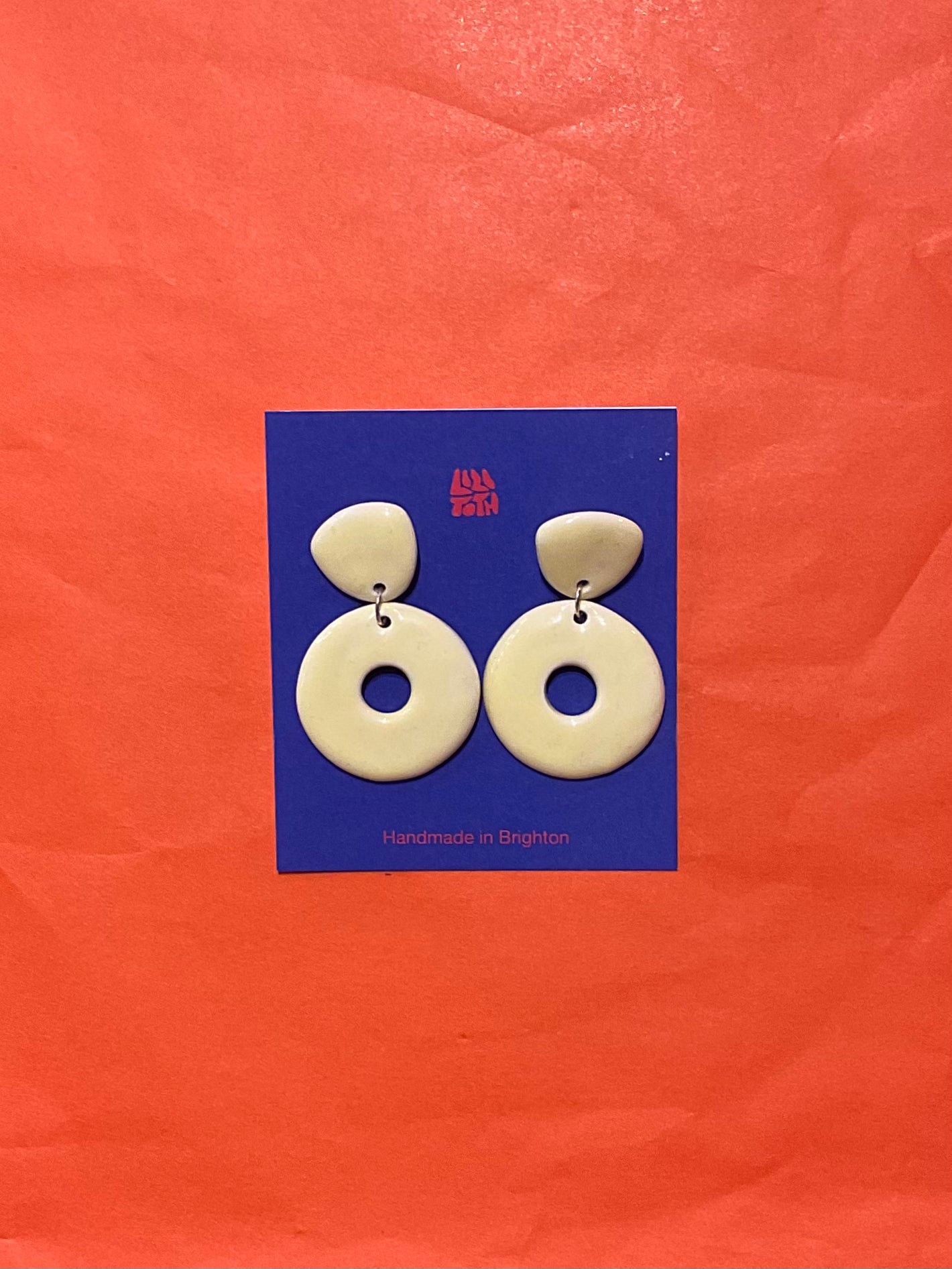 Pair of white circular earrings on a blue card with 'Alfie & Dally' branding against an orange background.