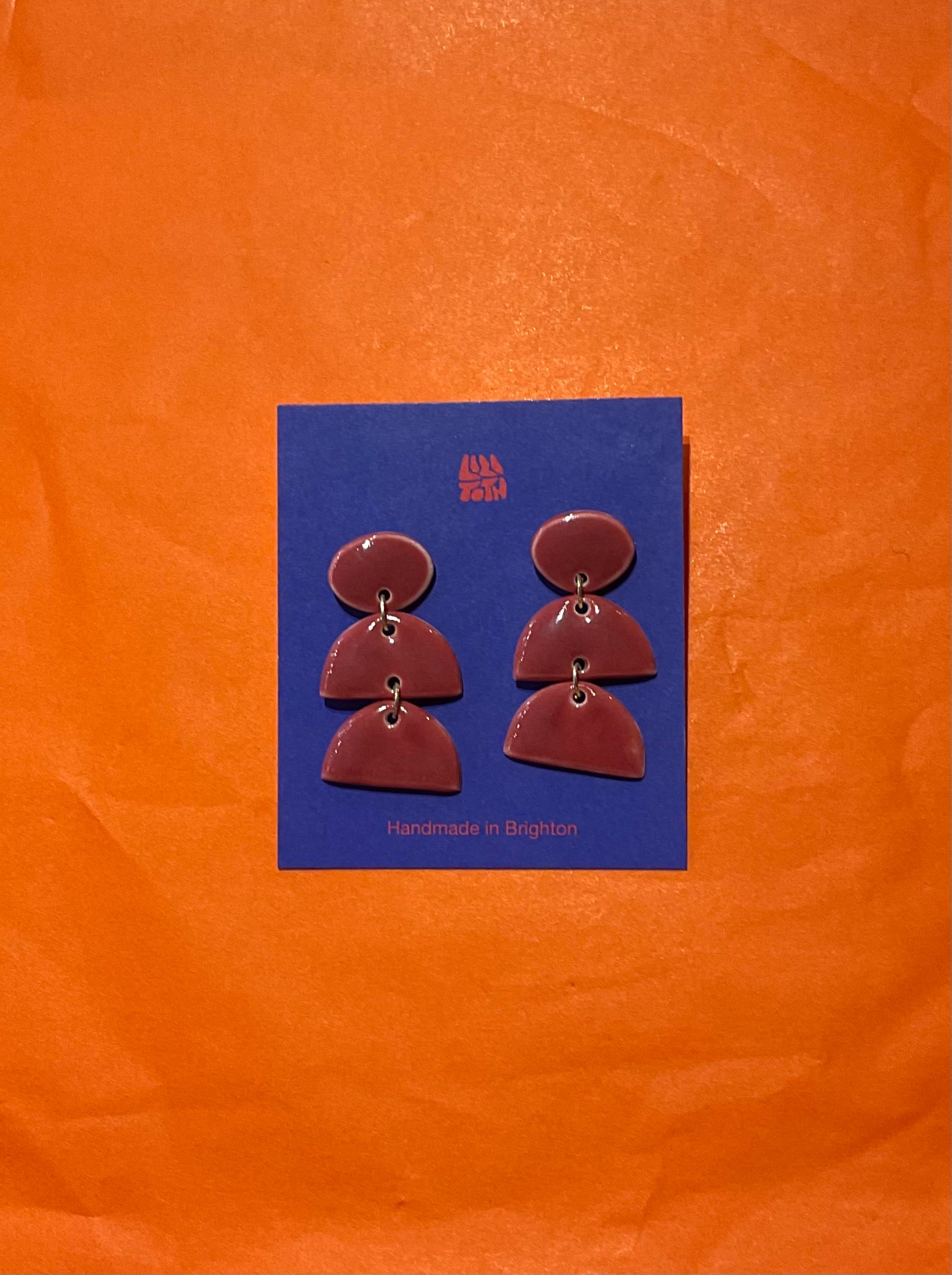 Pair of earrings on a blue card with 'All the Luck' branding against an orange background