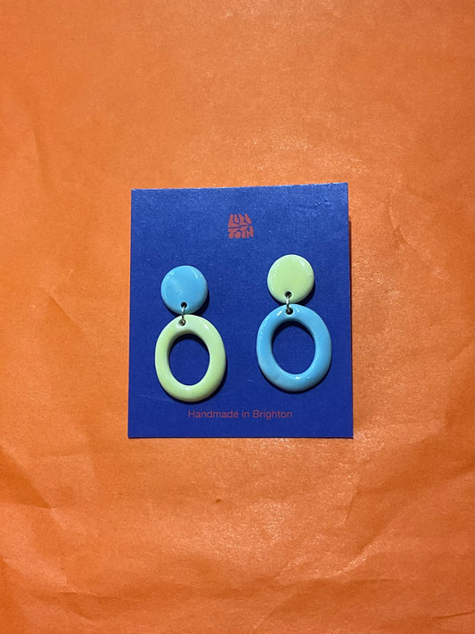 Pair of blue and green circular earrings on a blue card against an orange background