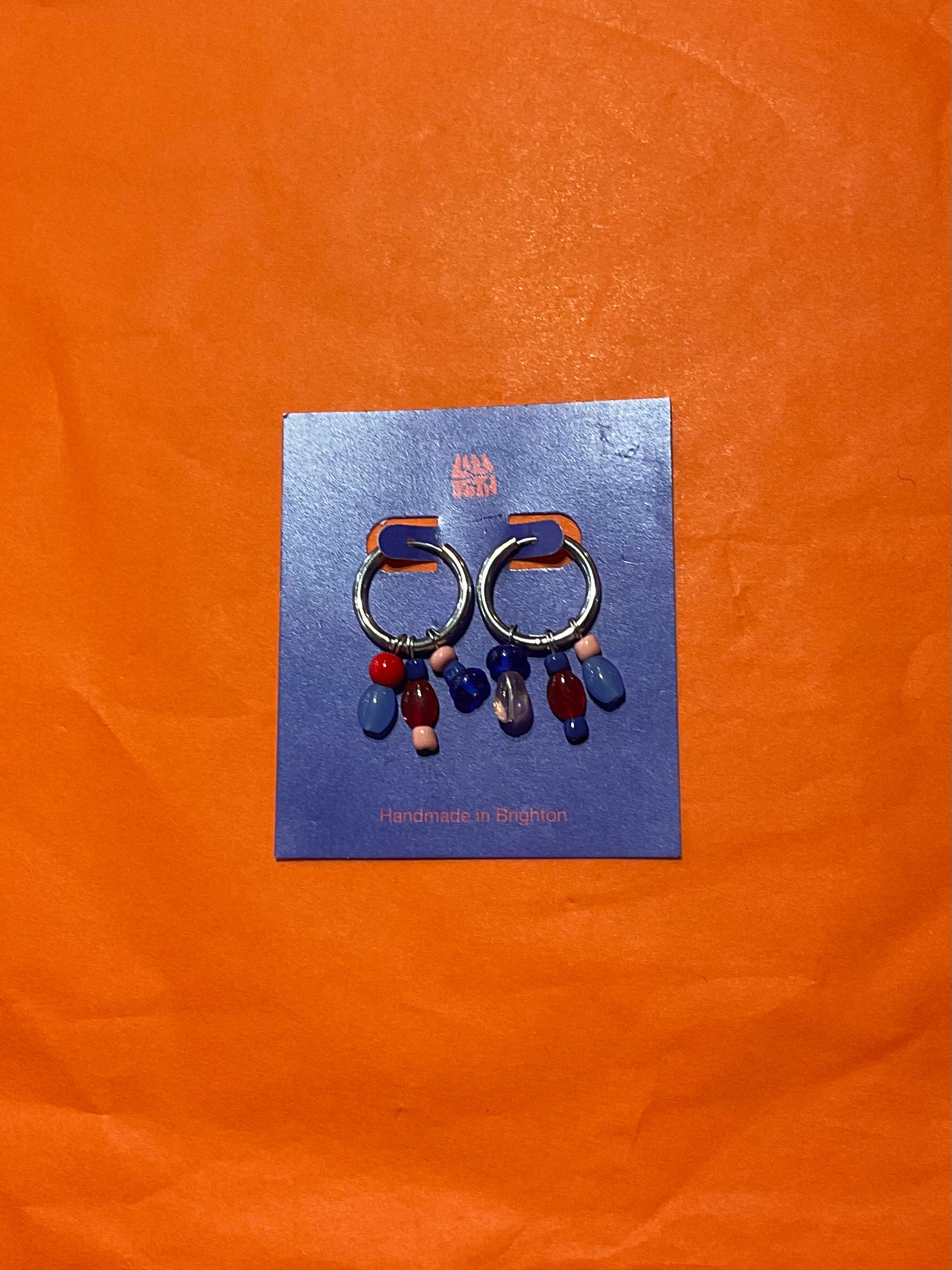 Earrings on a blue card with 'Bella' branding against an orange background
