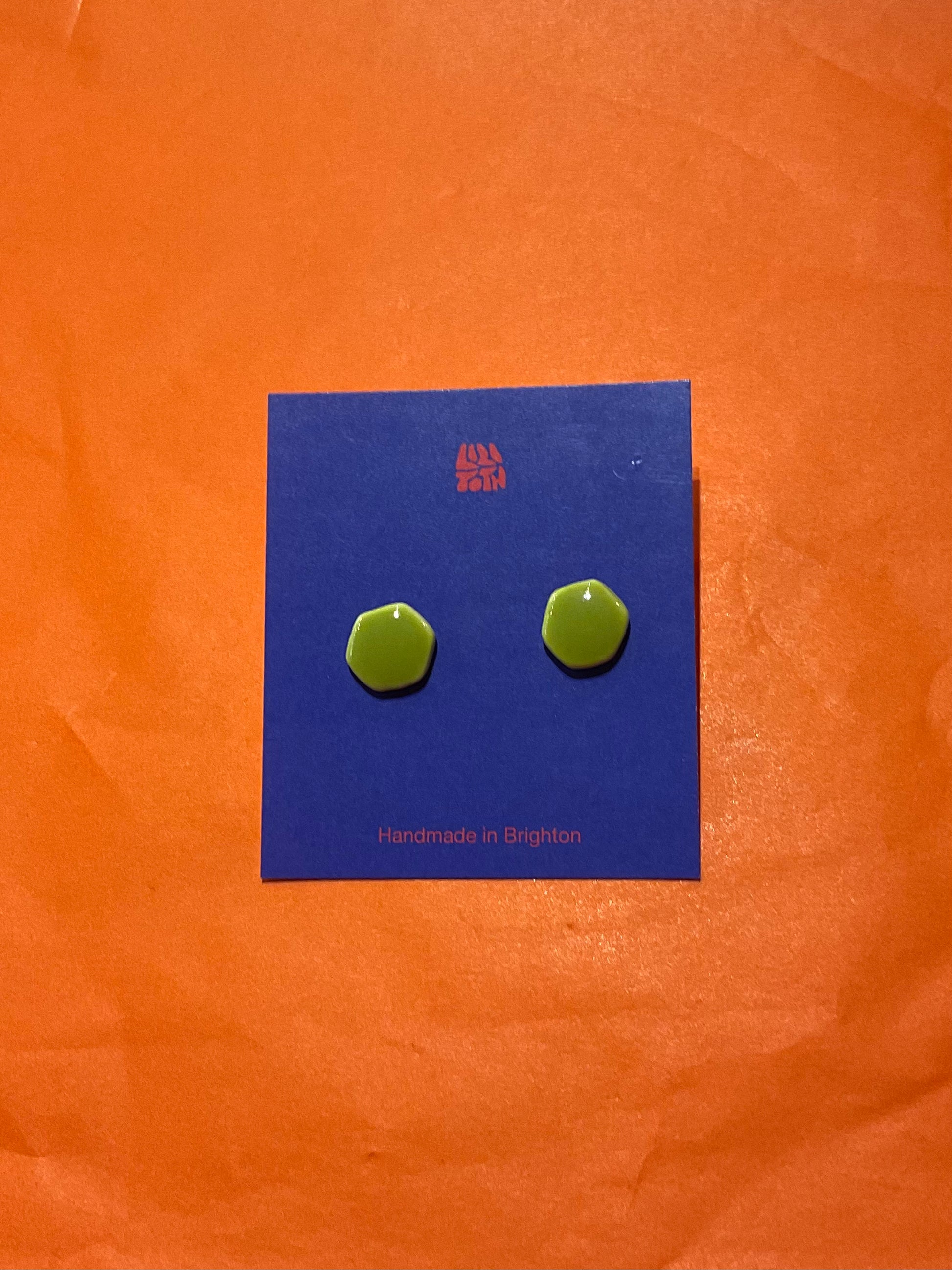 Green hexagonal earrings on a blue card with 'Handmade in England' text, against an orange background.