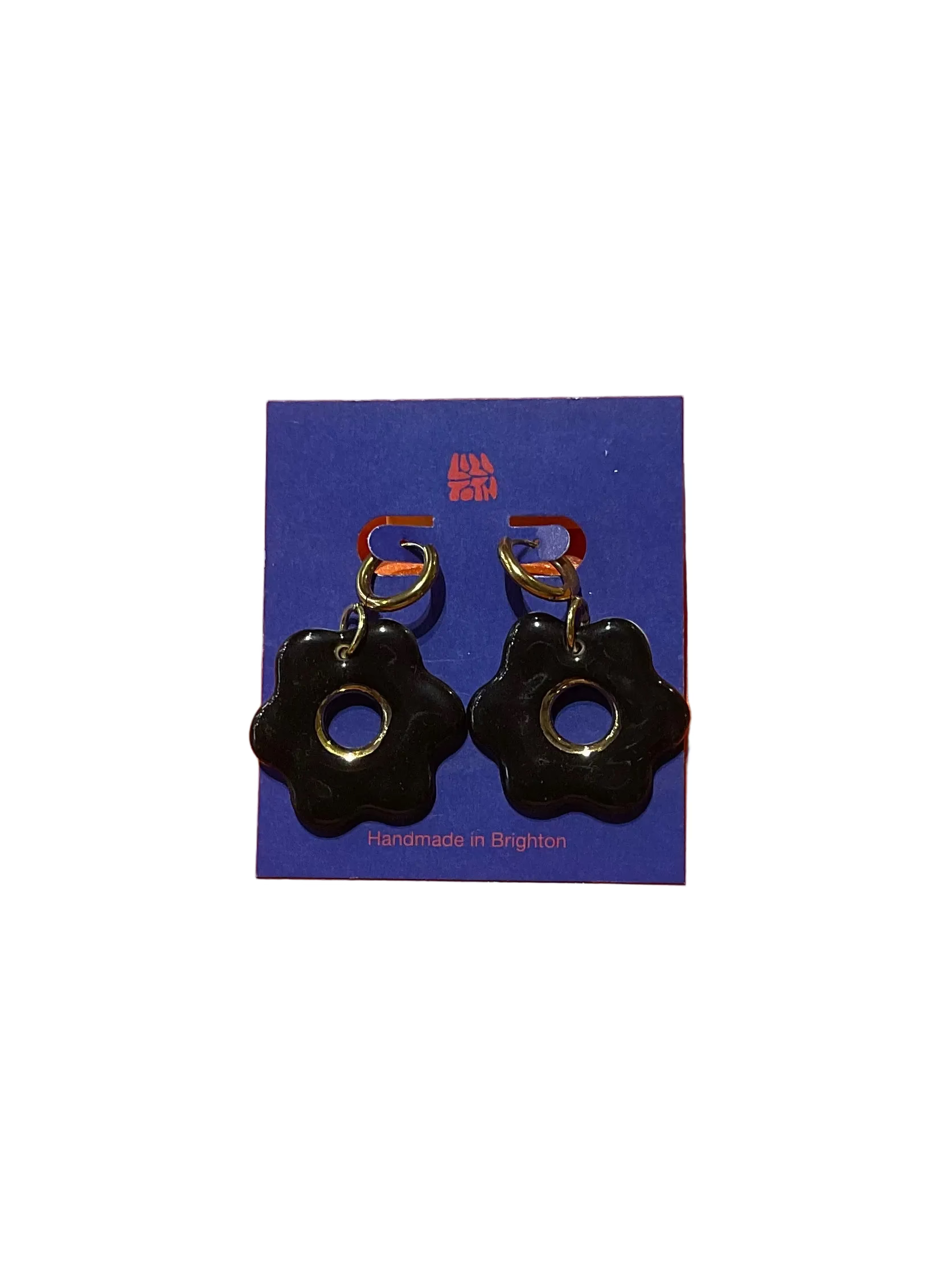 Black flower-shaped earrings on a blue card with 'Handmade in Brighton' text, against an orange background.