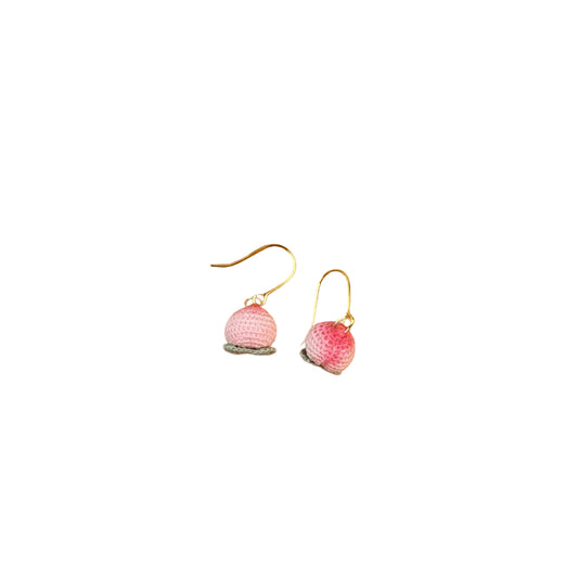 Pair of pink earrings on a wooden surface with a green leaf and white fabric background