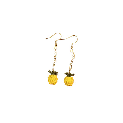 Pineapple-shaped earrings on a wooden tray with a white fabric background