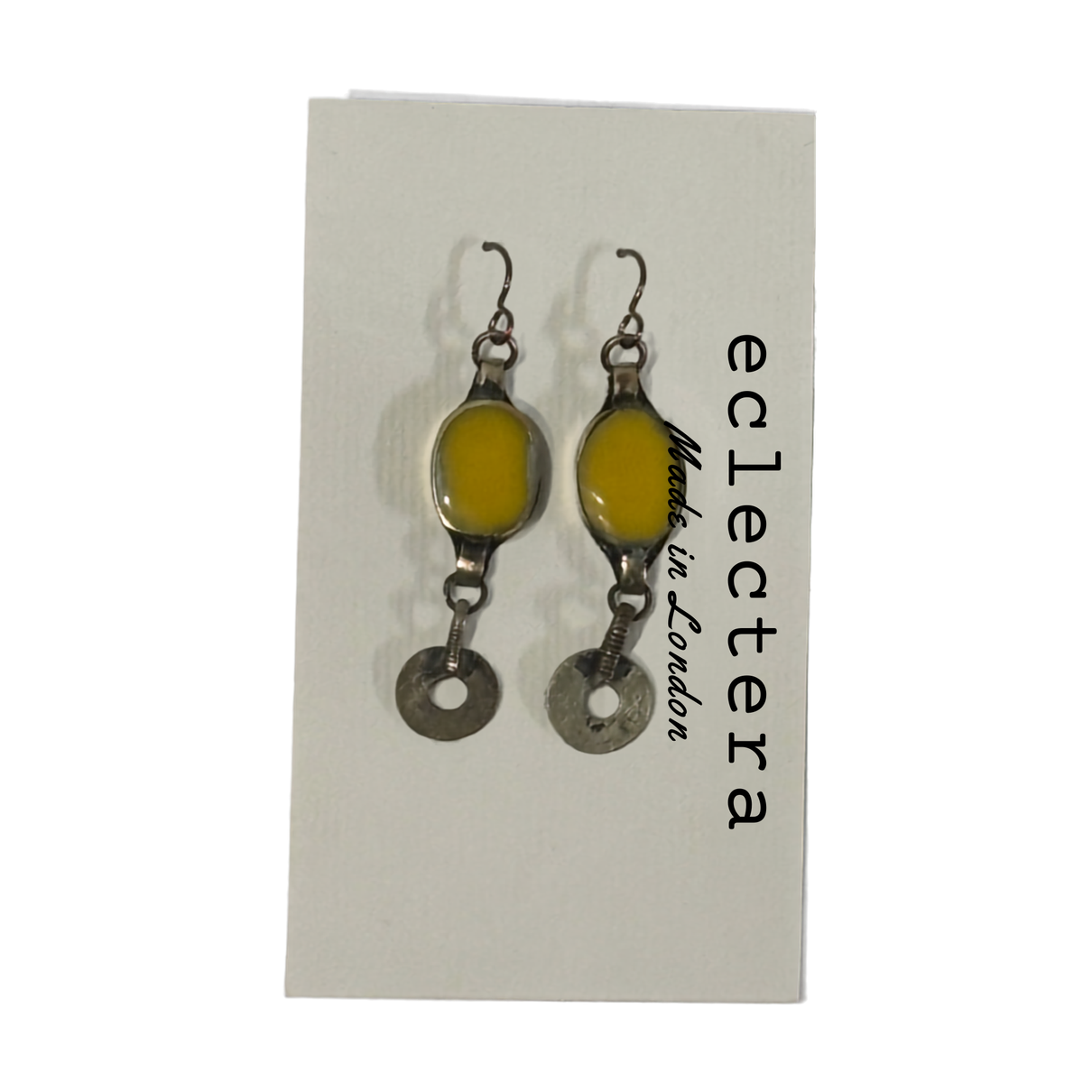 A pair of handmade dangle earrings with oval yellow resin centers and silver-toned metal charms, displayed on a white backing card printed with the brand name 'eclectera'.