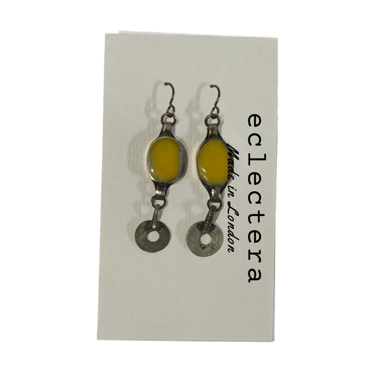 A pair of handmade dangle earrings with oval yellow resin centers and silver-toned metal charms, displayed on a white backing card printed with the brand name 'eclectera'.
