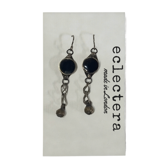 A pair of gothic-style dangle earrings with dark round stones and silver-toned chains, displayed on a white card printed with the brand name 'eclectera made in London'.
