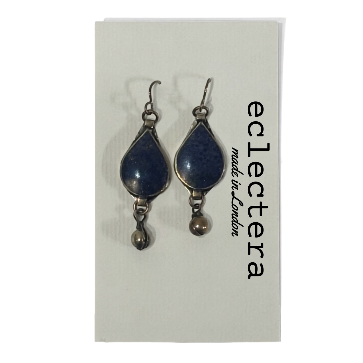 A pair of silver-toned dangle earrings with teardrop-shaped dark blue lapis lazuli stones and small dangling beads, displayed on a white card printed with the brand name 'eclectera made in london'.