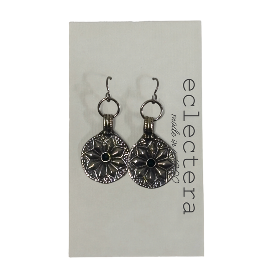 A pair of silver-toned dangle earrings with circular floral medallions and small black center stones, displayed on a white card labeled 'eclectera'.