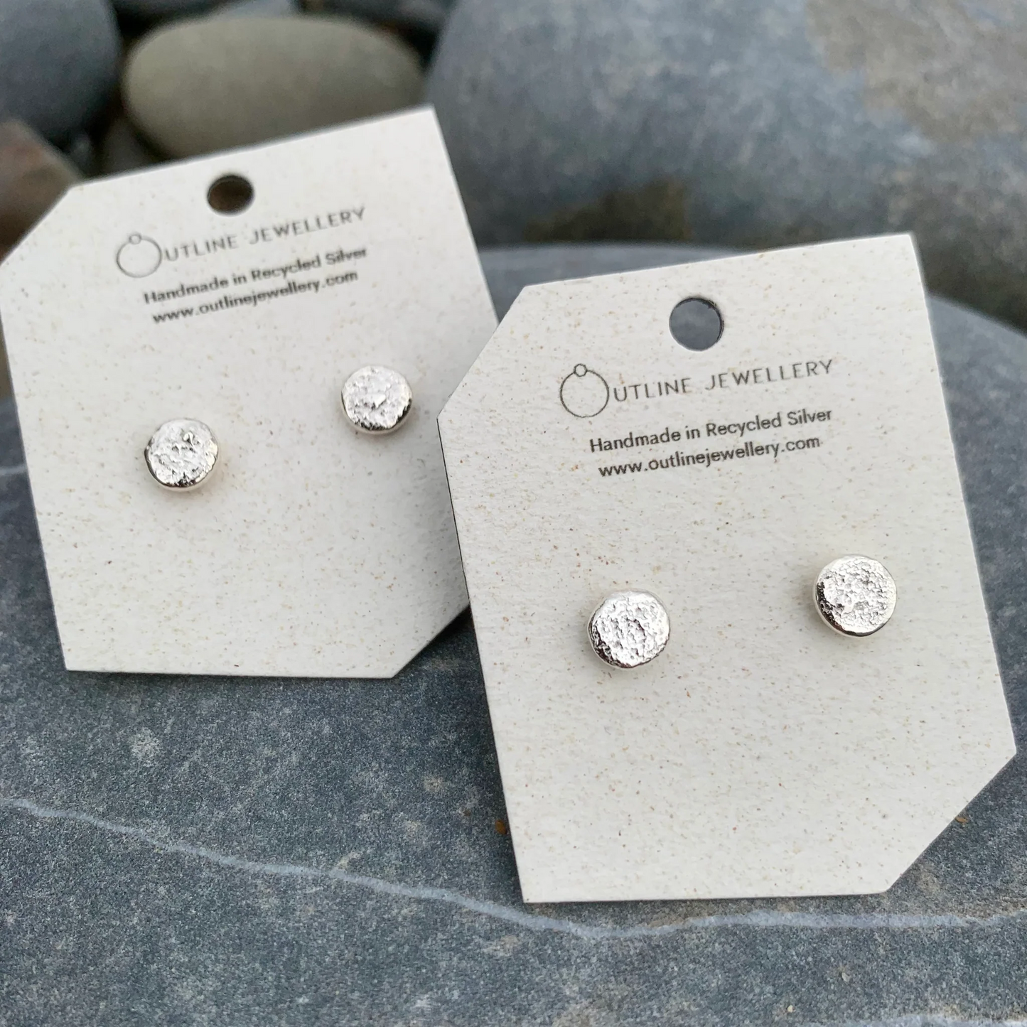 Pair of silver stud earrings on Outline Jewellery cards against a stone background