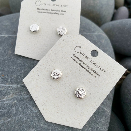 Silver earrings on display cards with 'Outline Jewellery' branding on a stone surface.