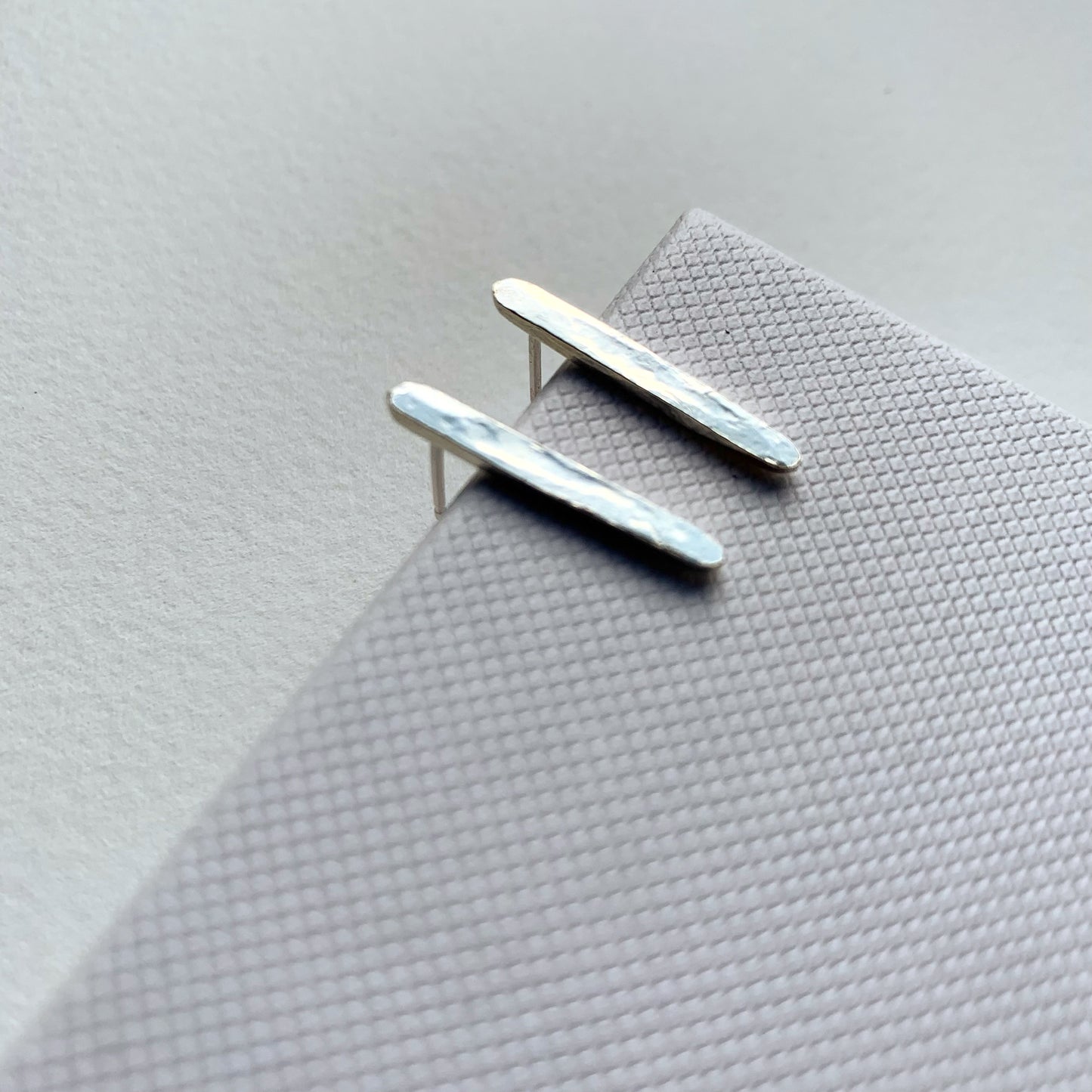 Pair of silver bar earrings on a textured gray surface