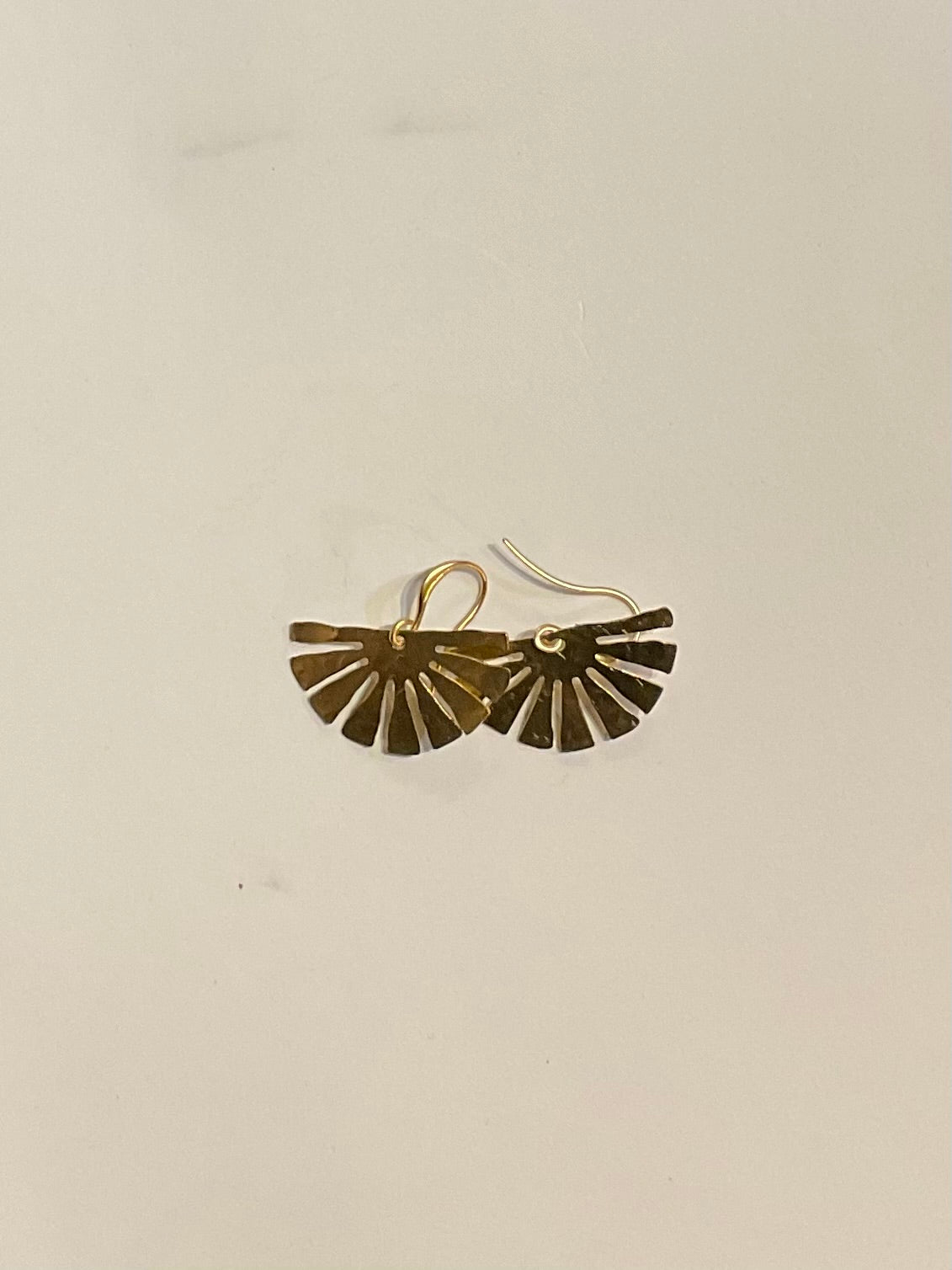 Gold fan-shaped earrings on a beige background