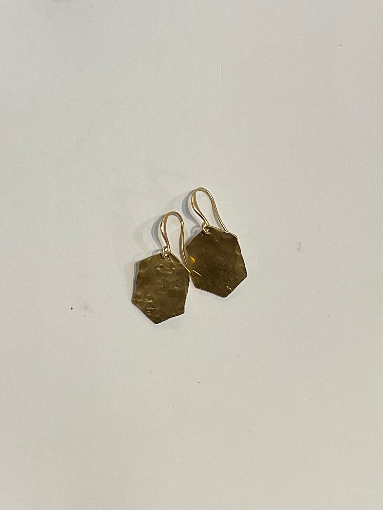 Hexagonal gold earrings on a light gray background