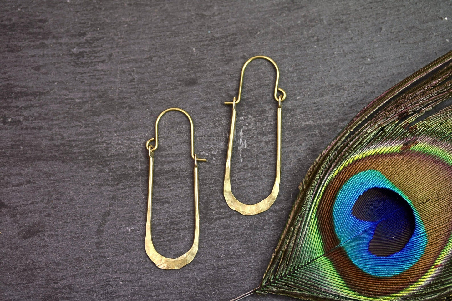 Gold hoop earrings on a dark surface with a peacock feather