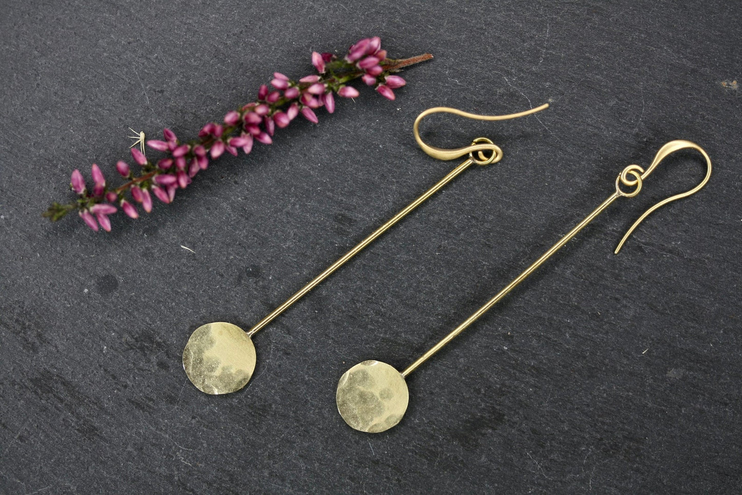Gold earrings on a dark surface with purple flowers