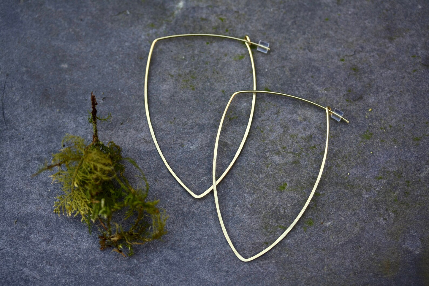 Gold hoop earrings on a textured gray surface with a small patch of green moss.