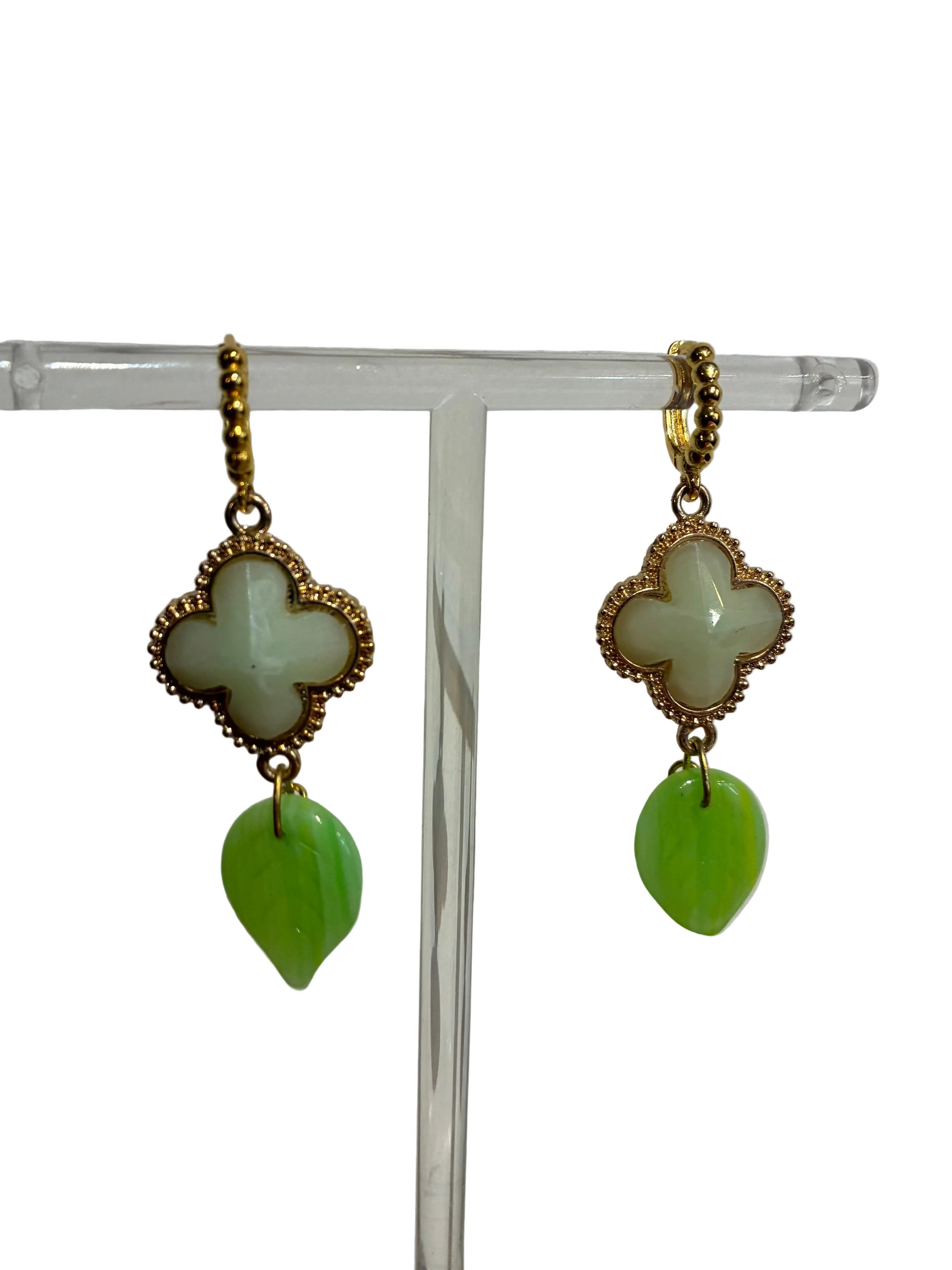 Pair of earrings with gold clover-shaped tops and green leaf-like bottoms on a clear stand against a white background.