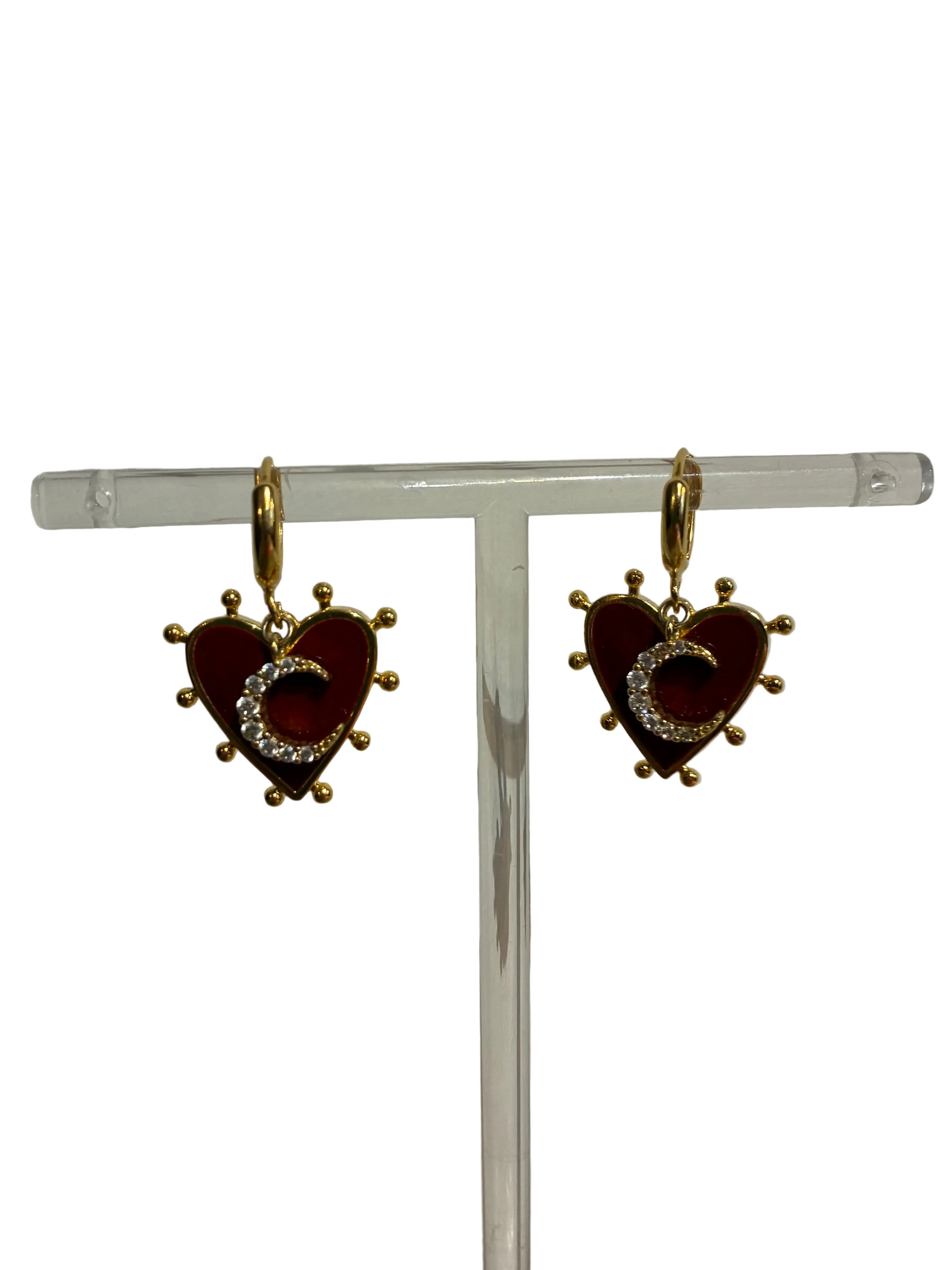 Heart-shaped earrings with red center and gold accents on a clear stand against a white background