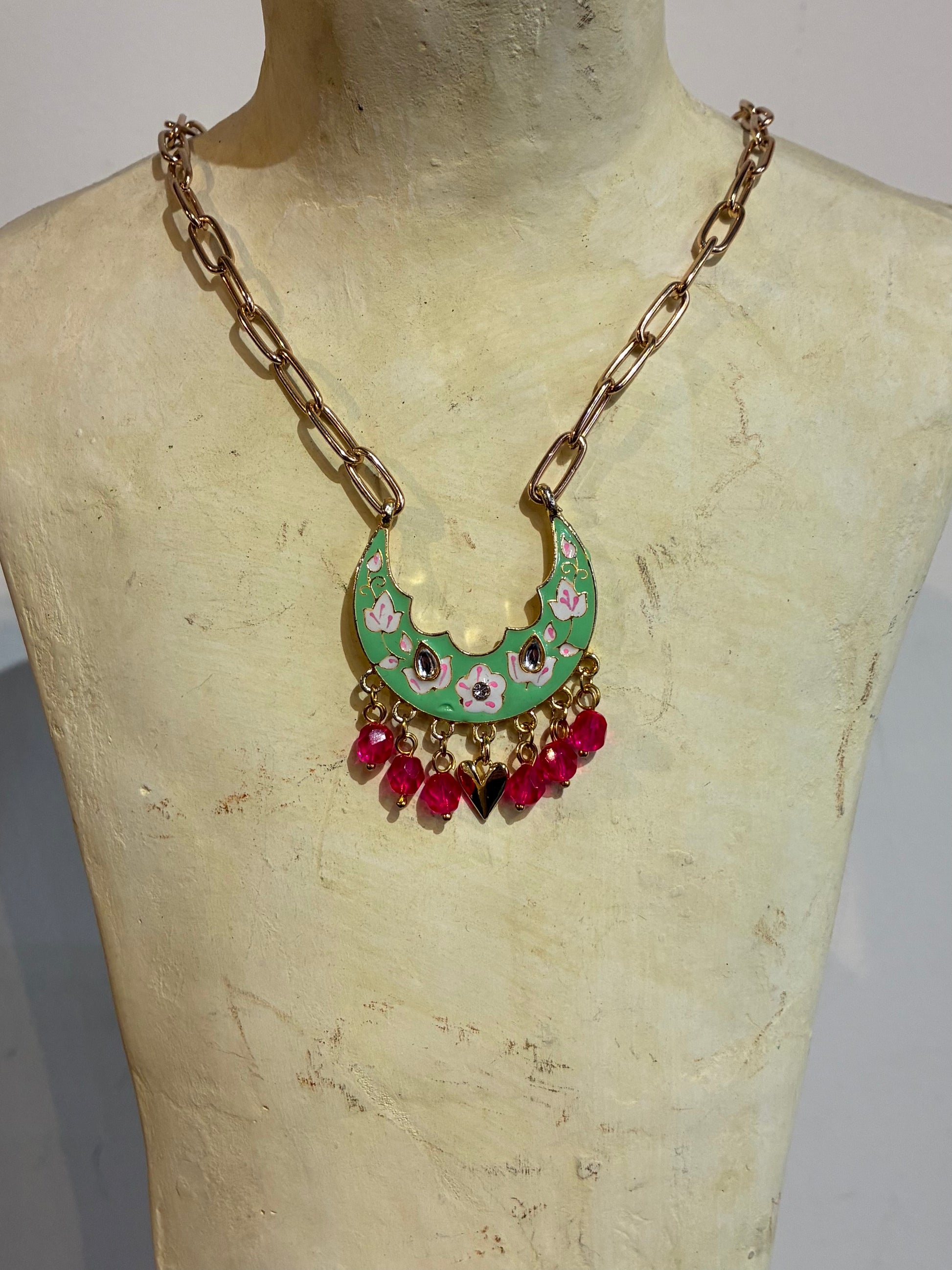 Necklace with floral pendant and red beads on a mannequin bust.