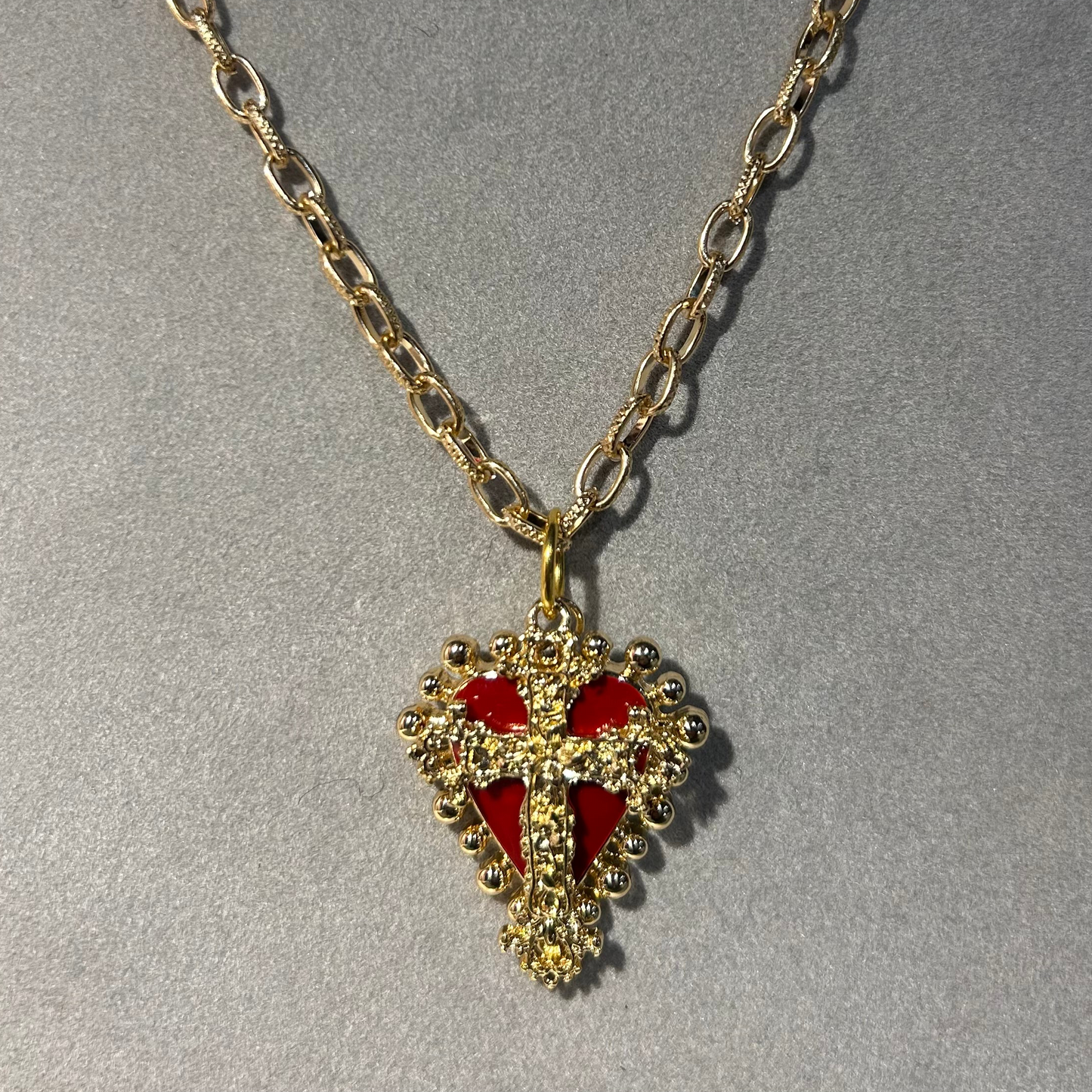 Gold necklace with a heart-shaped pendant featuring red accents on a gray background