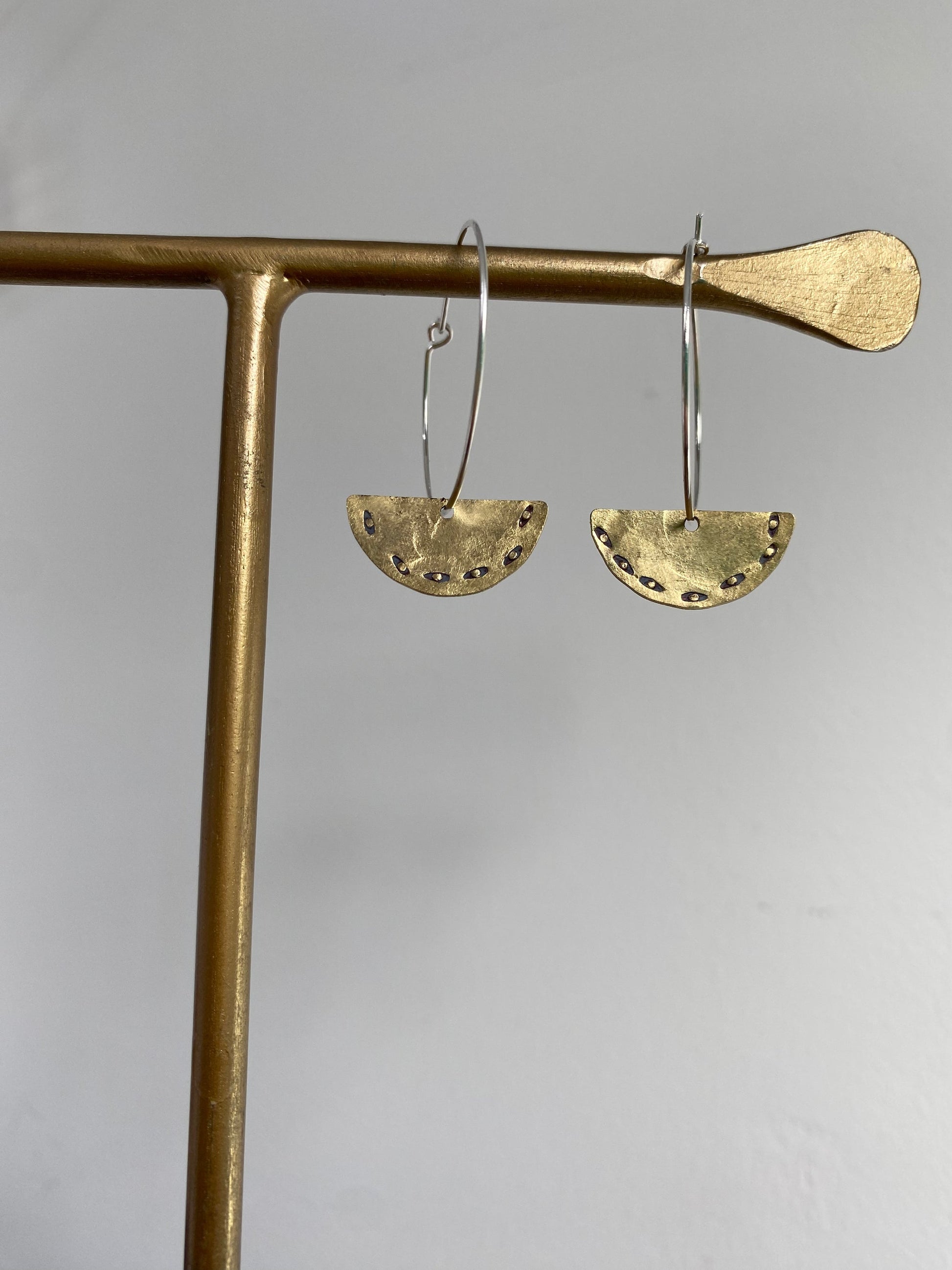 Gold hoop earrings with half-circle designs hanging on a gold stand against a gray background