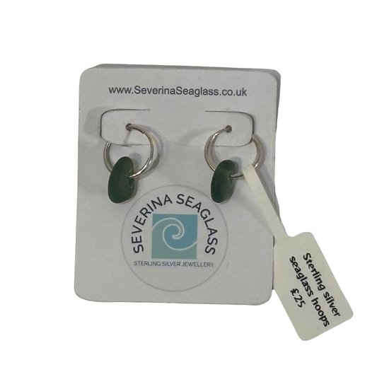 A pair of sterling silver seaglass hoop earrings with dark green oval stones, displayed on a white Severina Seaglass brand backing card with a price tag attached.