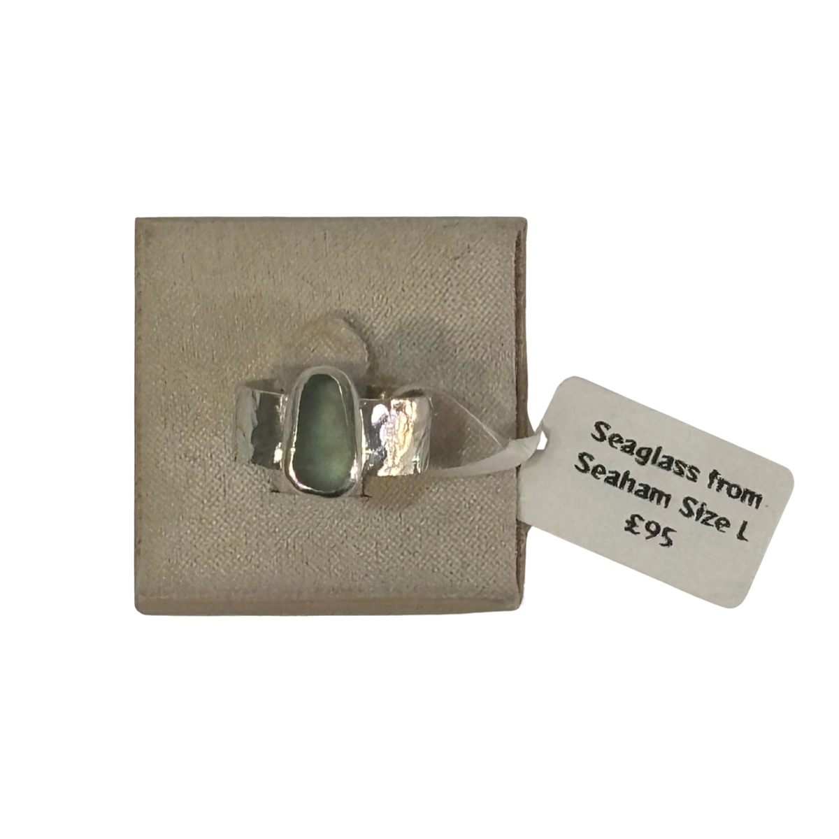 A silver ring with a polished seaglass stone, presented on a textured beige display card with a white price tag attached.