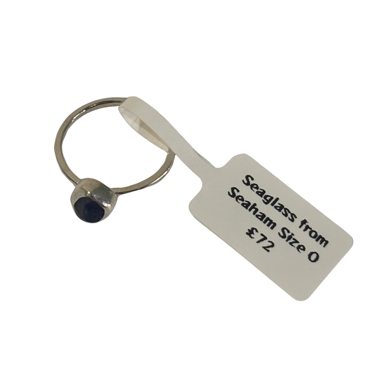A single seaglass ring with a small oval dark blue stone set in a silver-toned bezel, attached to a white paper tag that reads 'Seaglass from Seaham Size 0 £72'.